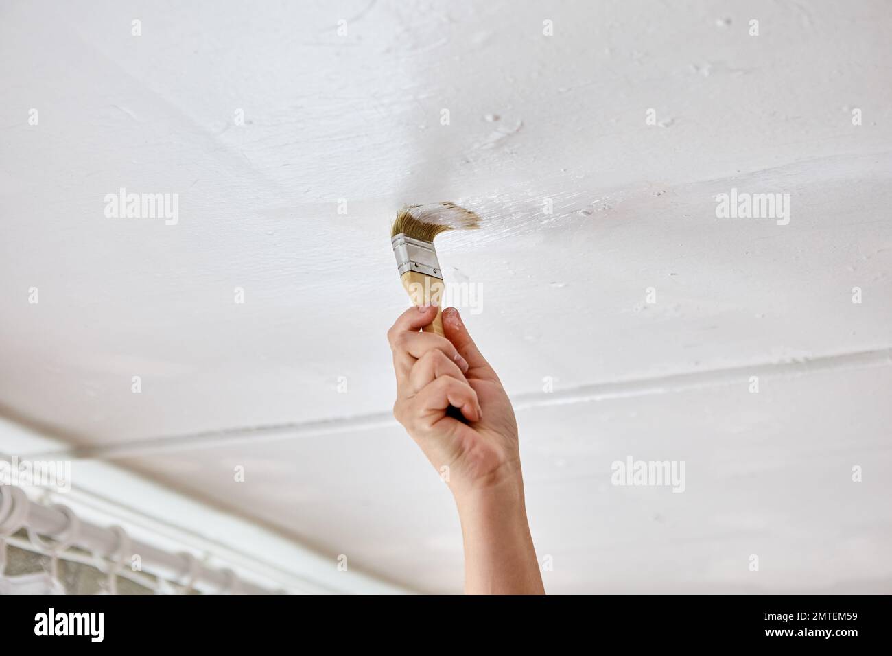 Using paintbrush to touch up ceiling with white paint, house painter