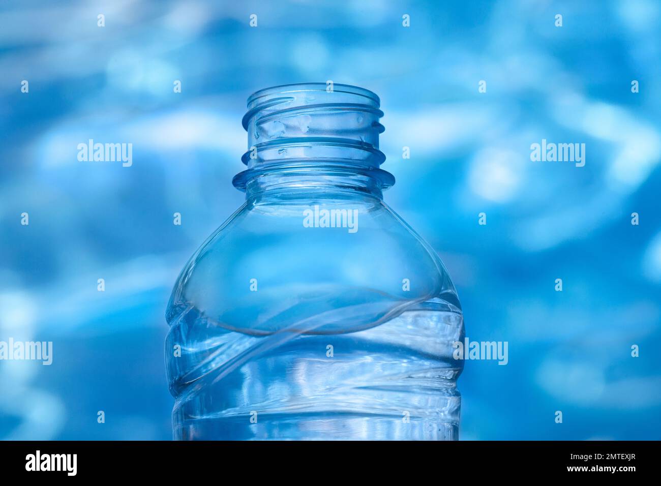 Close up view of plastic bottle full of water against blue color water background with light reflections Stock Photo