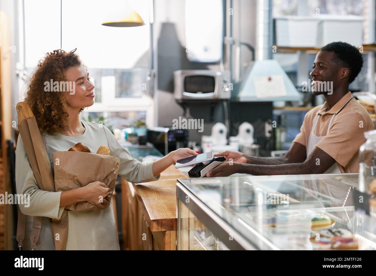 Happy woman using contactless payment app when paying for bread in local bakery Stock Photo