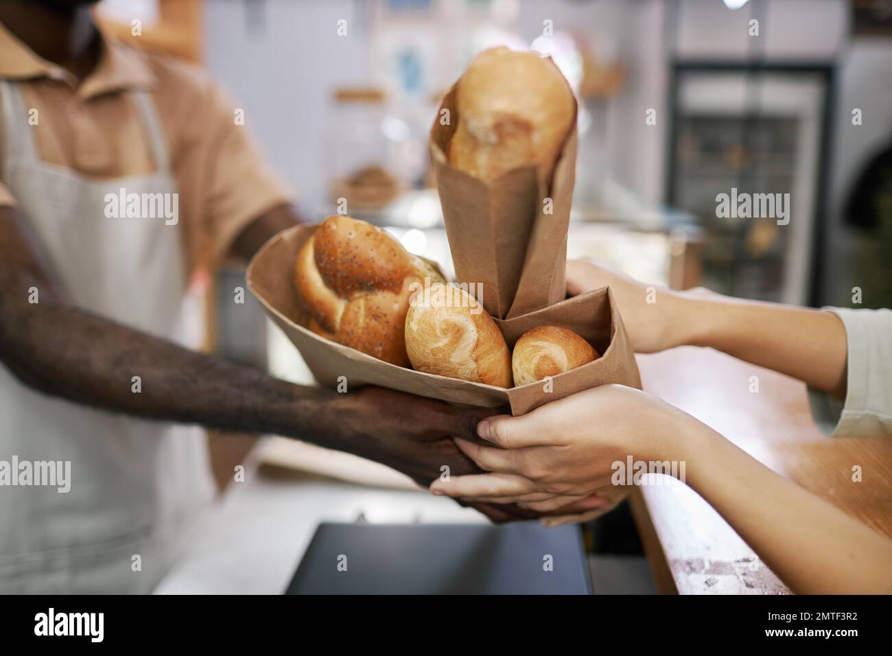 Hands of bakery worker giving packagers with fresh baguettes to customer Stock Photo