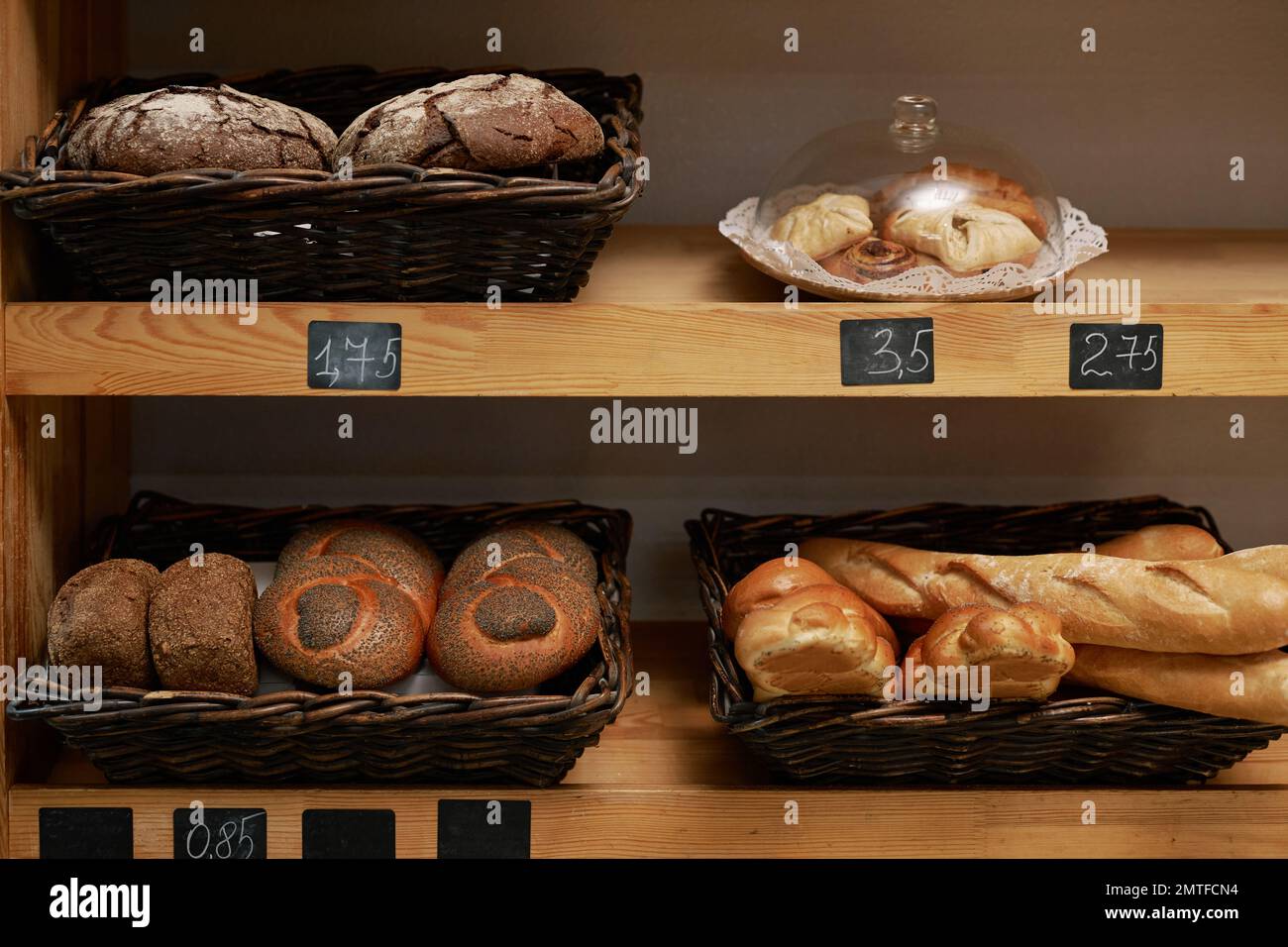 Baskets with various types of bread and price tags on shelves in bakery Stock Photo