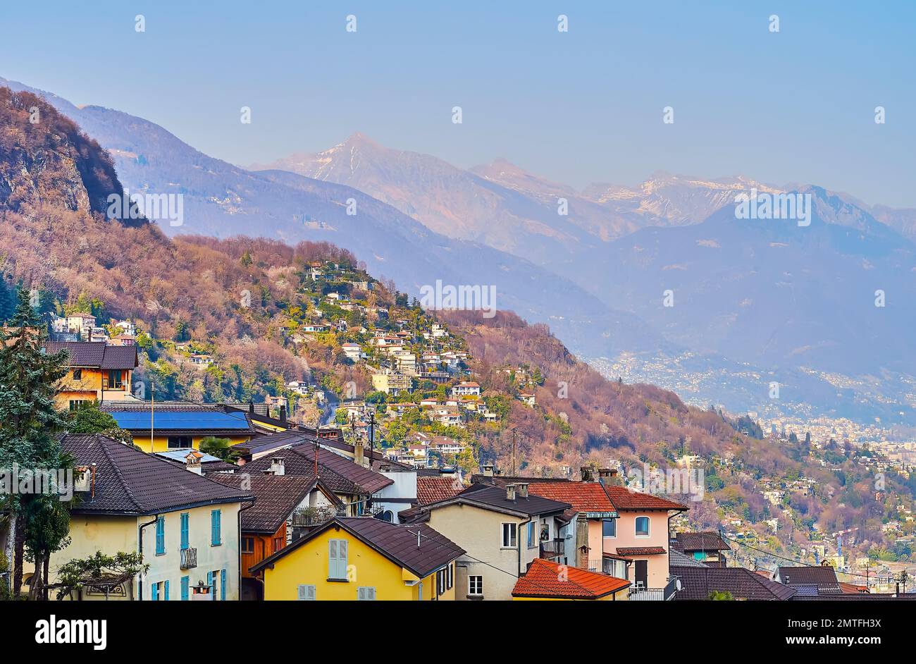 Alpine slopes, covered with small houses, forests and topped with snow from the mountain village of Ronco sopra Ascona, Switzerland Stock Photo