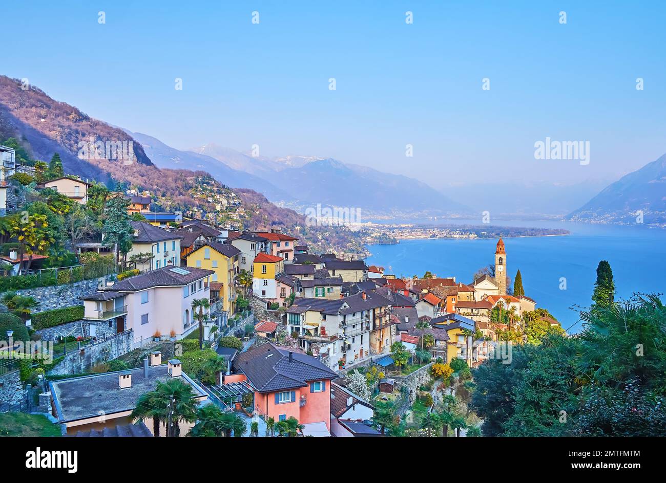 The beautiful Alpine landscape with houses of Ronco sopra Ascona, blue Lake Maggiore and hazy mountains in light of evening sun, Switzerland Stock Photo