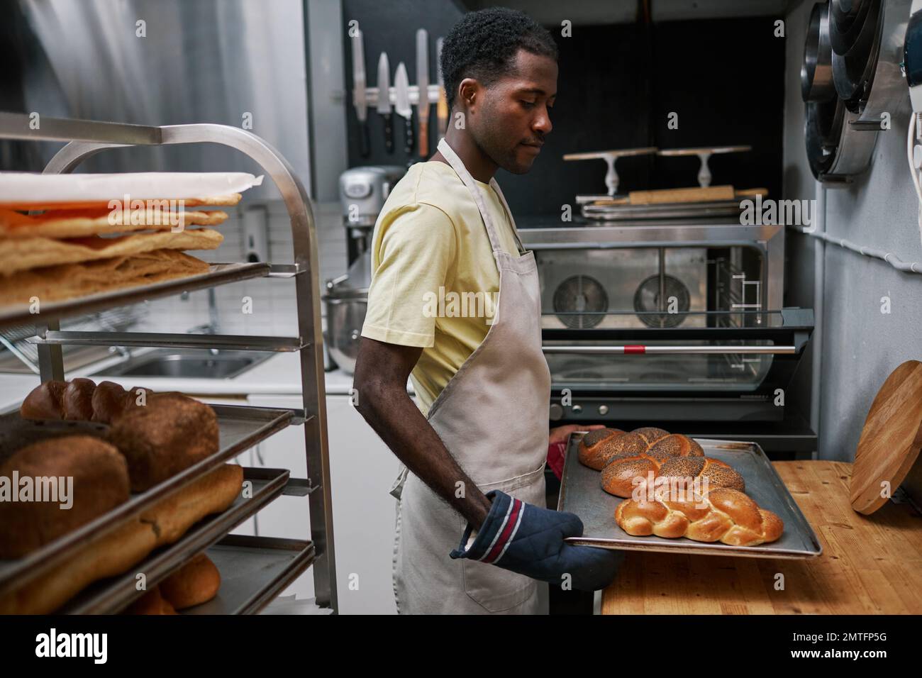Bakery worker putting hot tray with freshly baked bread on table to let it cool Stock Photo