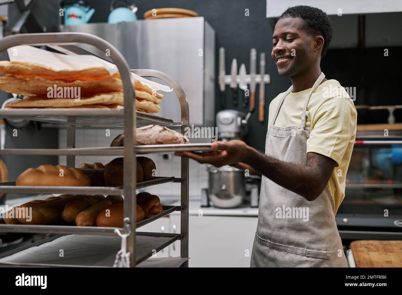 Smiling man putting trays with freshly made bread in bakers rack Stock Photo