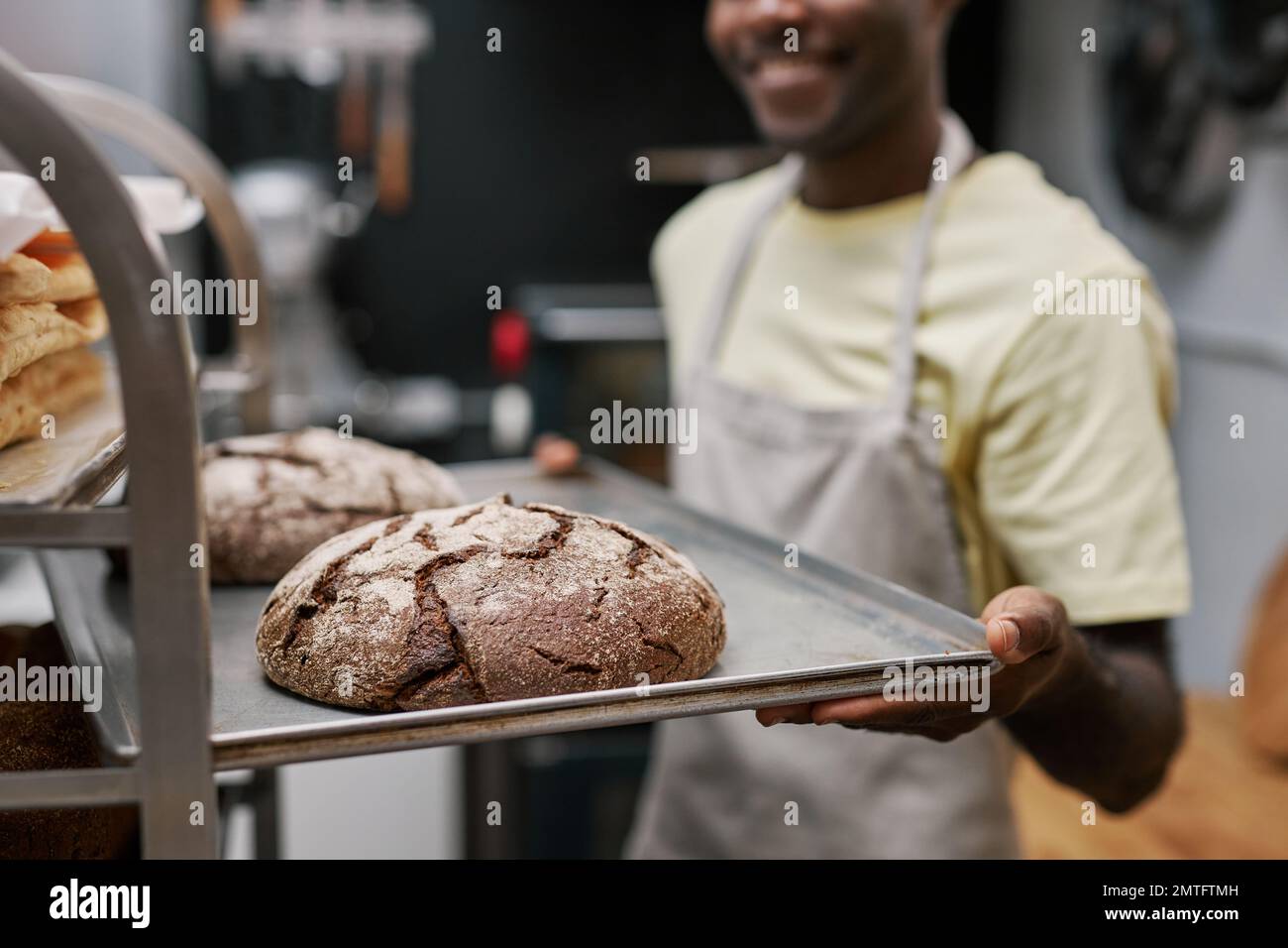 Closeup image of smiling baker putting tray with freshly baked bread in bakers rack Stock Photo