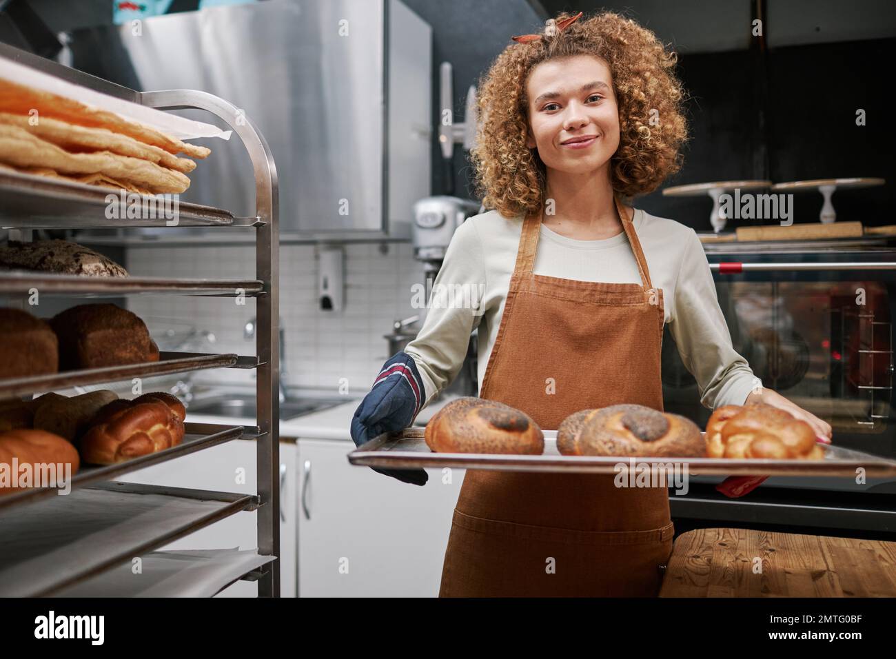 Portrait of positive baker holding tray with fresh braided bread with poppy seeds Stock Photo