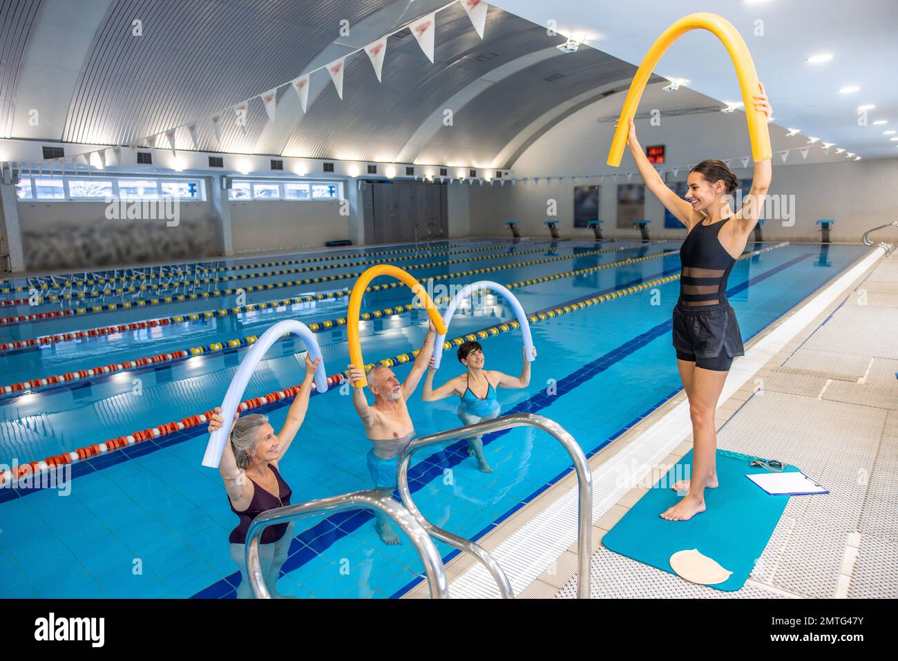 Dark-haired young coach showing exercises with float noodles to group of people Stock Photo