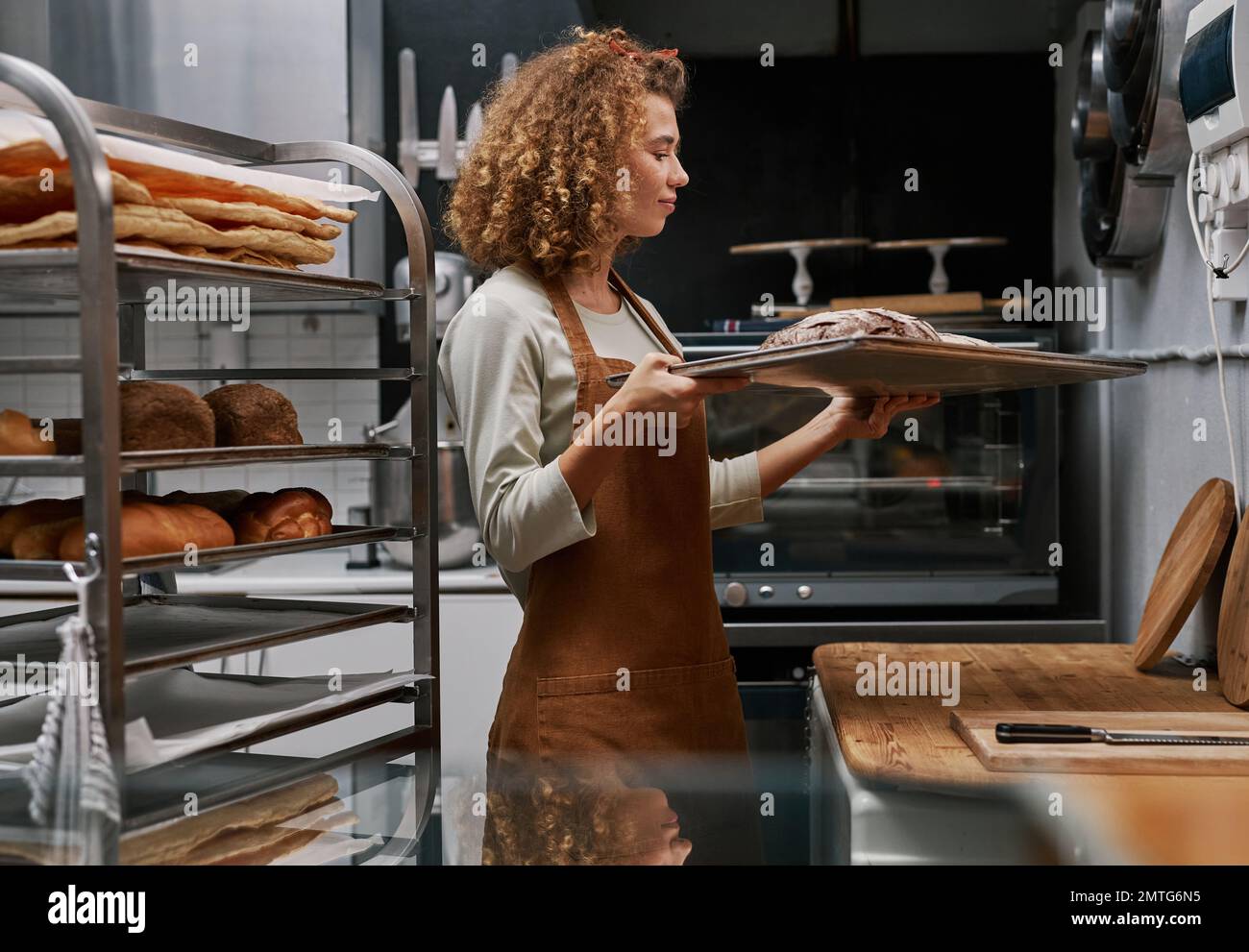 Happy baker looking at fresh loafs on tray she baked for selling Stock Photo