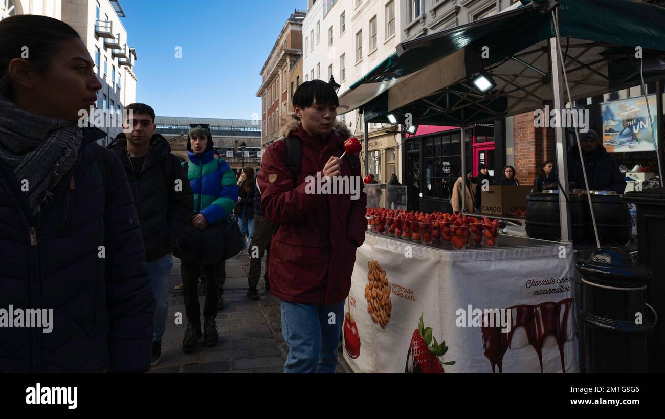 London - 02 27 2022: chocolate strawberry and candy apple vendor on James Street in Covent Garden with customer and woman looking strange Stock Photo