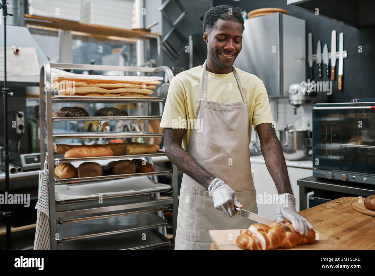 Happy Black baker cutting freshly baked bread in thin slices Stock Photo