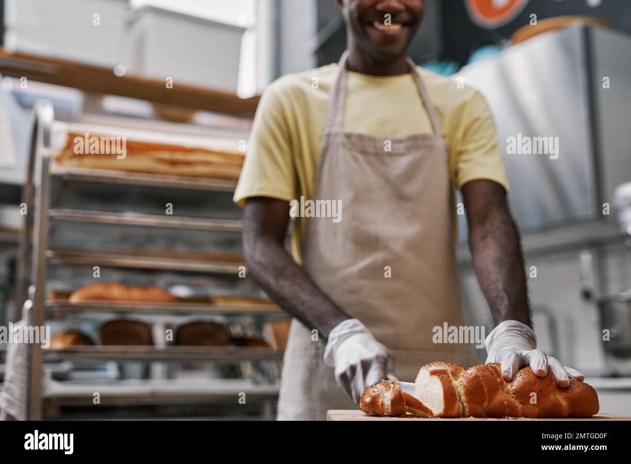 Smiling baker cutting braided bread with poppy seeds for customer Stock Photo
