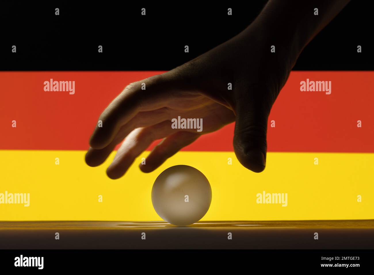 The hand picks a table tennis white ball in front of Germany flag Stock