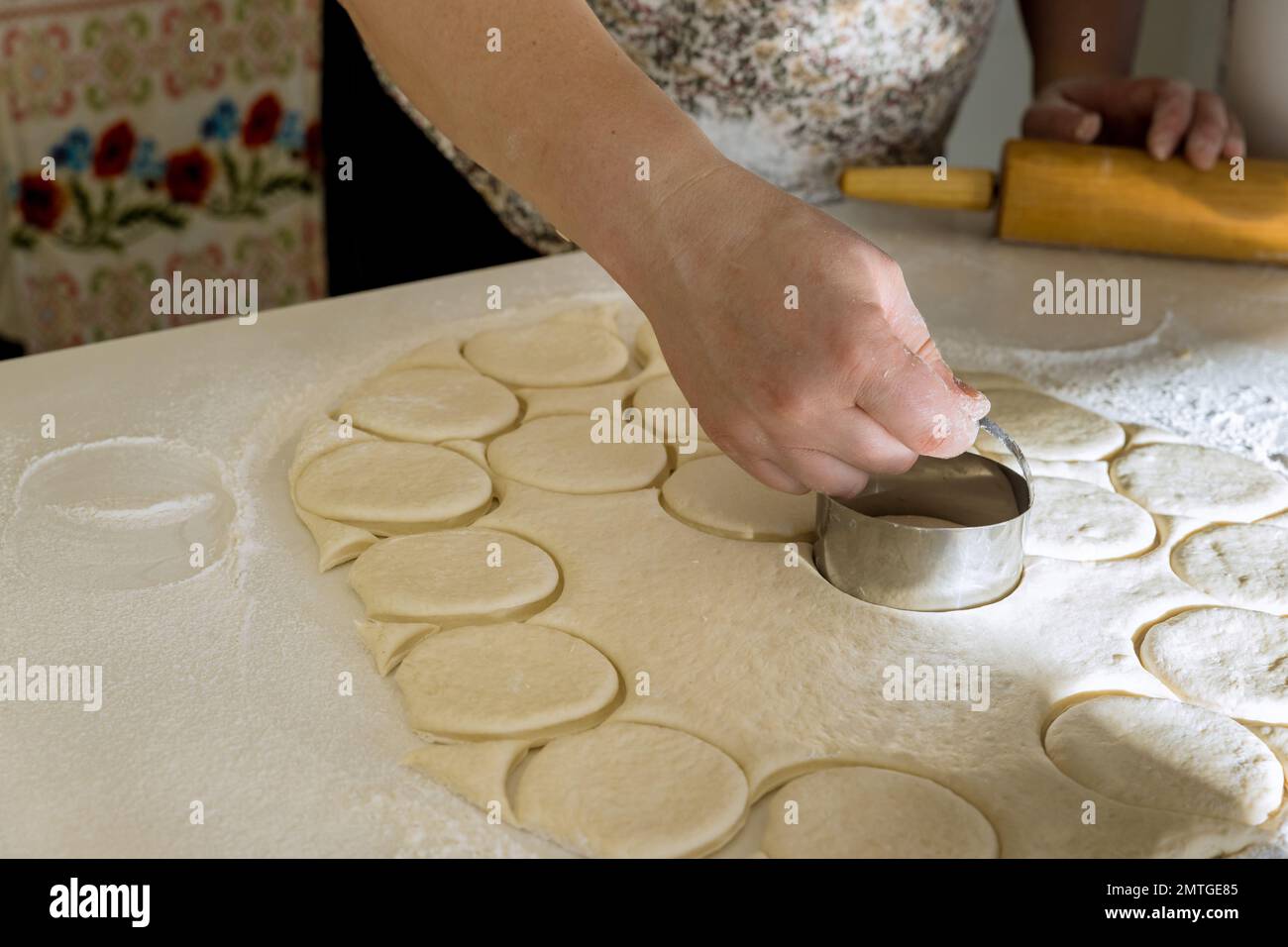 Raw homemade dough for donuts that has been cut into round pieces with rolling pin on bakery work table Stock Photo