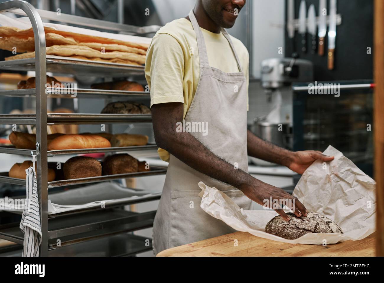 Cropped image of bakery worker wrapping bread in paper for customer Stock Photo