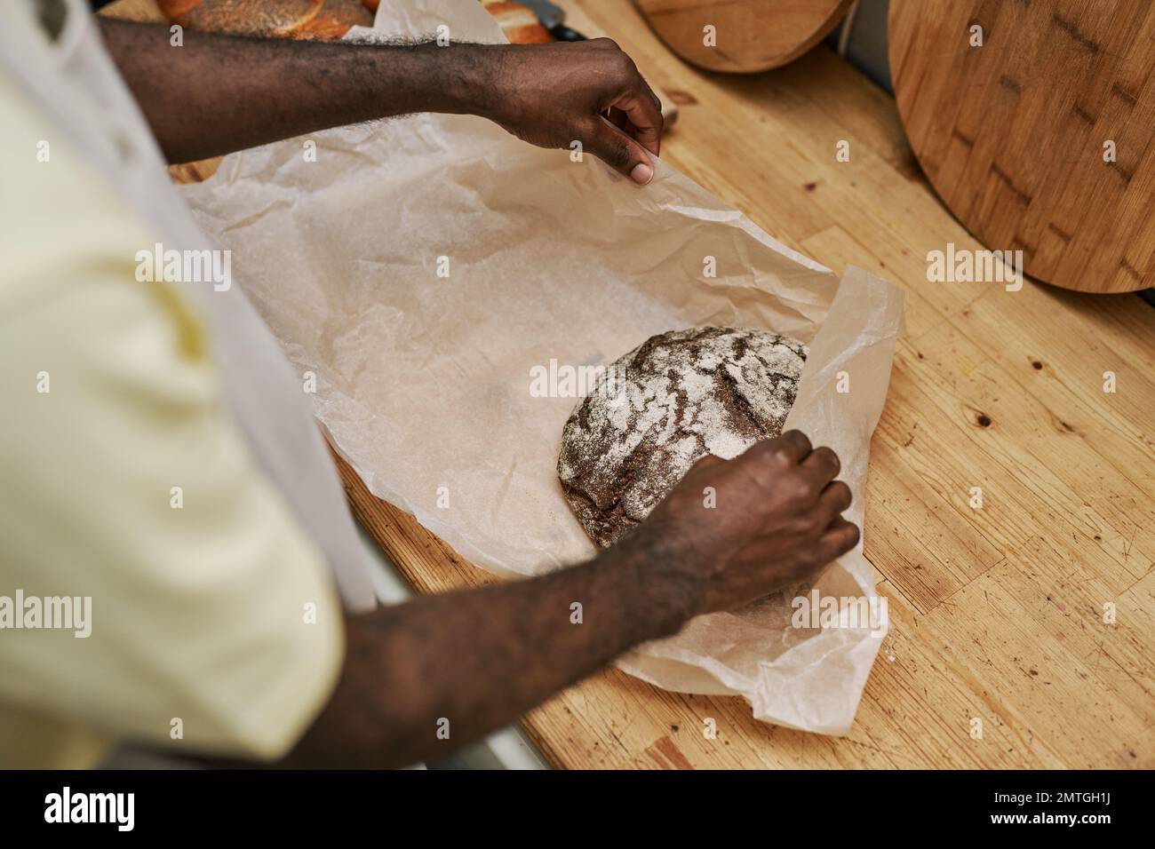 Hands of bakery worker wrapping loaf of rye bread in paper Stock Photo