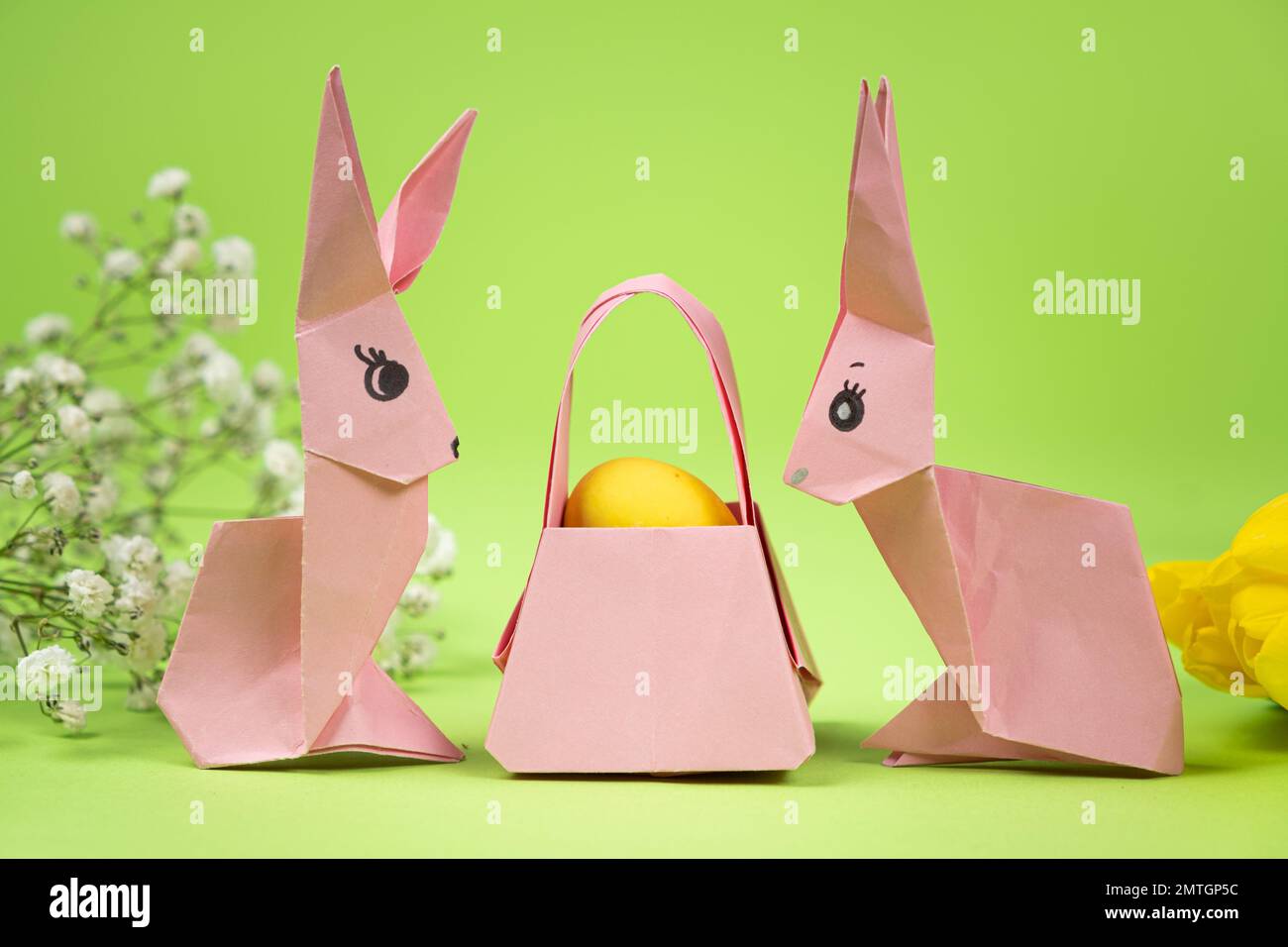 Easter origami - two paper bunnies and an egg, green background. Crafts for the holiday, do it yourself. Stock Photo