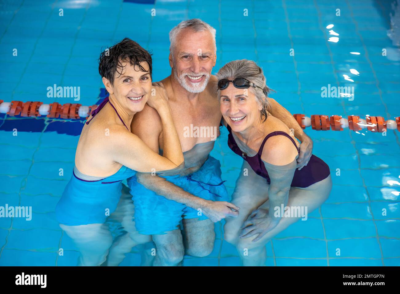 Senior man and two women standing in the water at the swimming pool Stock Photo