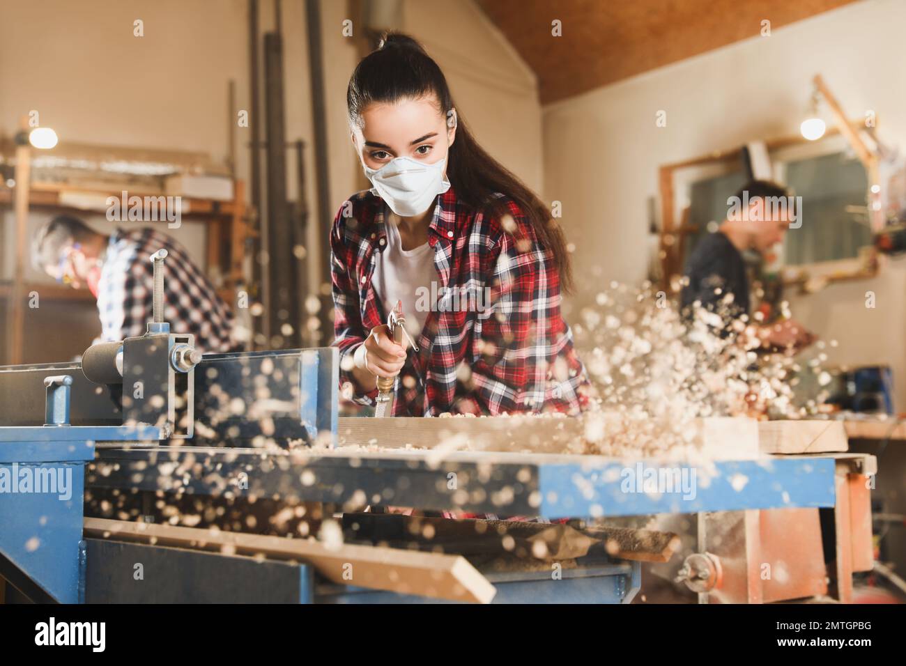 Female carpenter cleaning surface planer with air blow gun in workshop ...