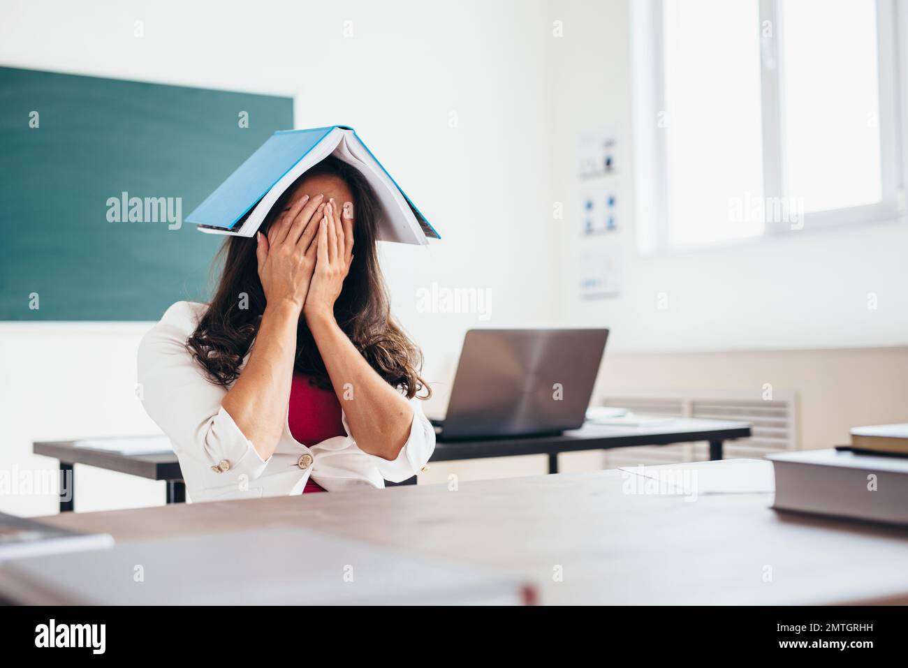 Tired female student sitting at the table with a book on her head. Stock Photo