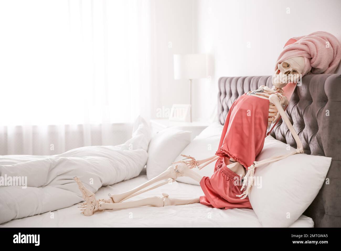 Human skeleton in silk pajamas and towel sitting on bed indoors Stock ...