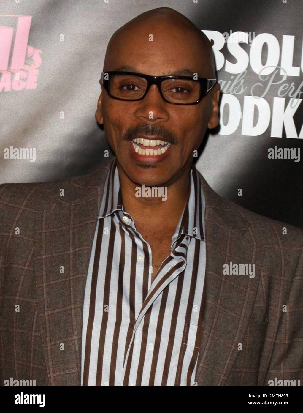 RuPaul looks sharp in a brown suit with striped shirt and glasses, a