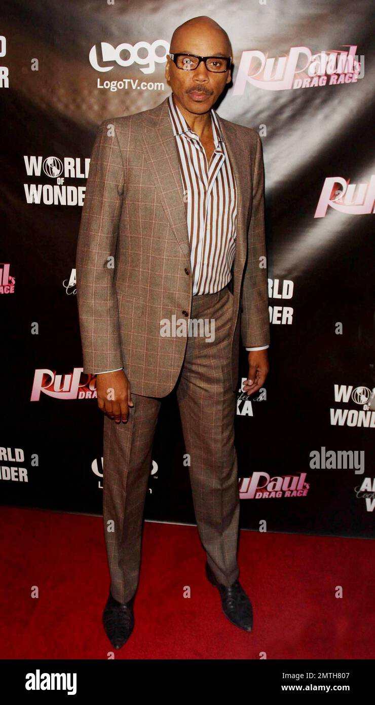 RuPaul looks sharp in a brown suit with striped shirt and glasses, a