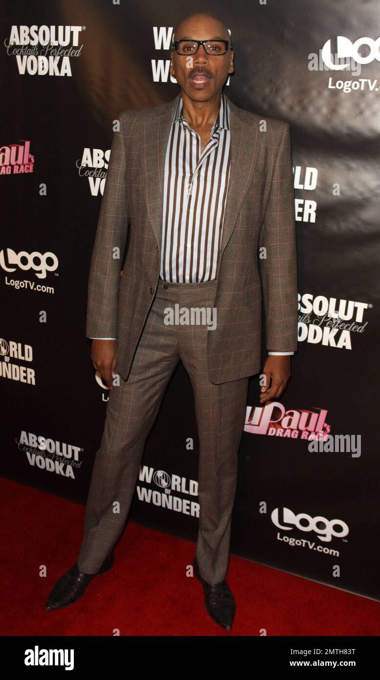 RuPaul looks sharp in a brown suit with striped shirt and glasses, a