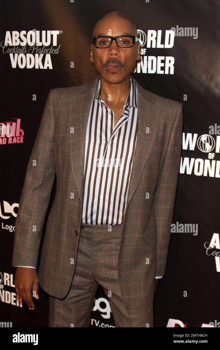 RuPaul looks sharp in a brown suit with striped shirt and glasses, a
