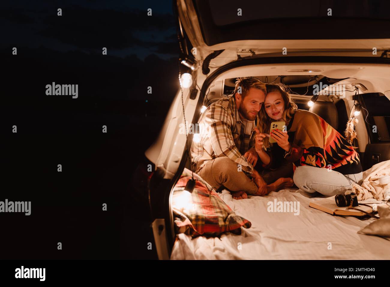 Happy young white couple using cellphone and lying together in car outdoors Stock Photo
