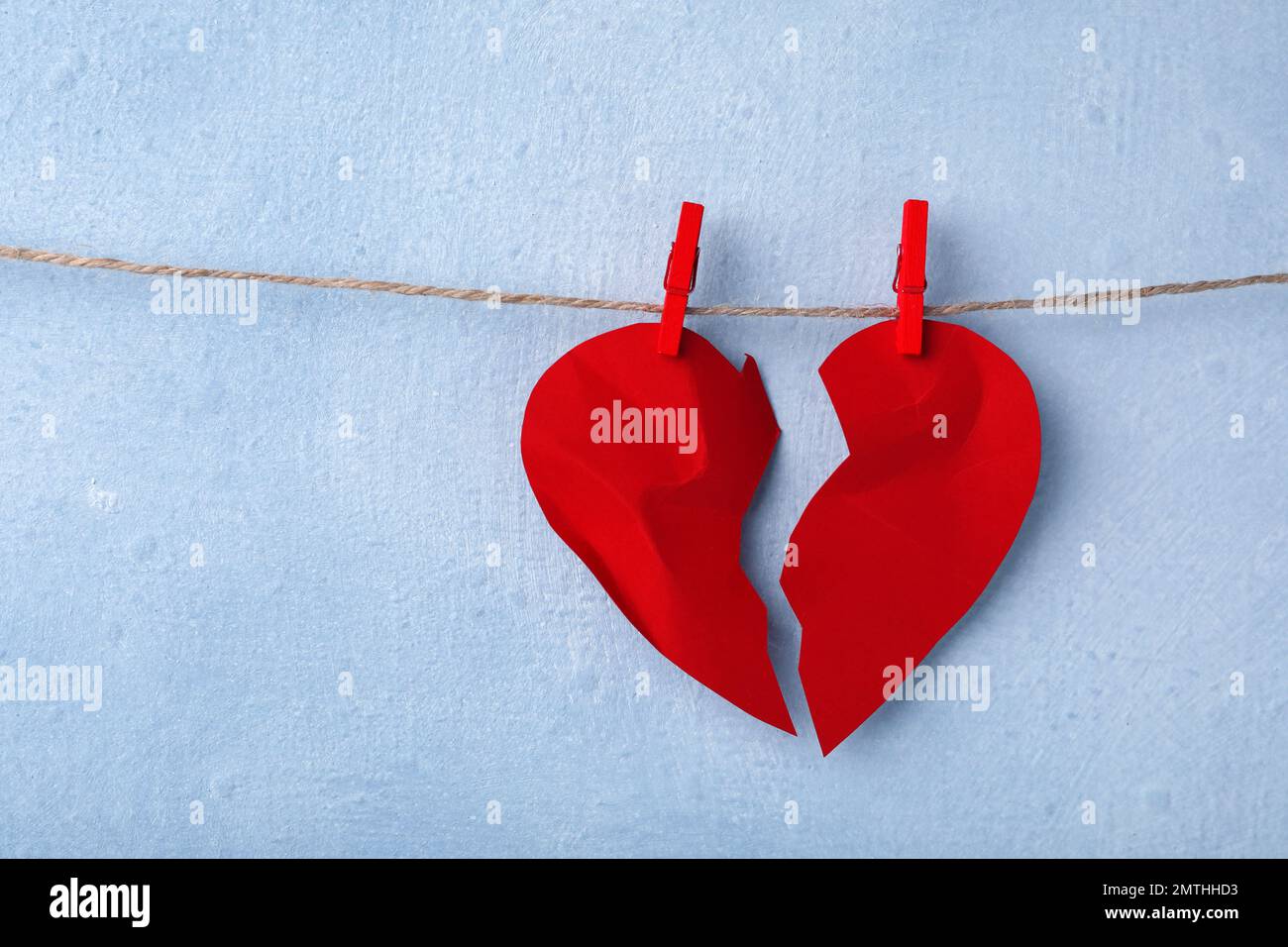 Halves of torn paper heart pinned on laundry string near light wall, space for text. Relationship problems concept Stock Photo