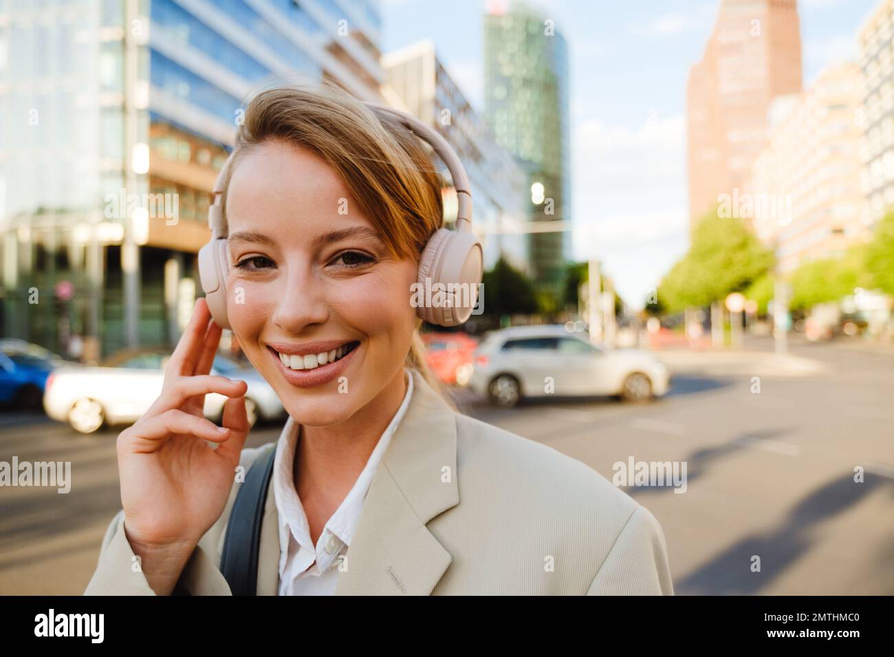Young white woman smiling and using headphones while walking on city street Stock Photo