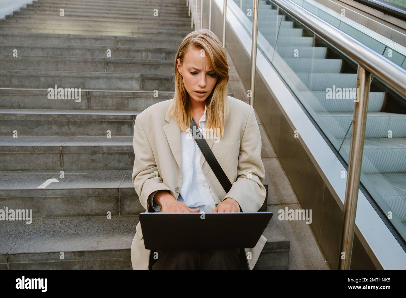 Young white serious woman using laptop while sitting on stairs outdoors Stock Photo