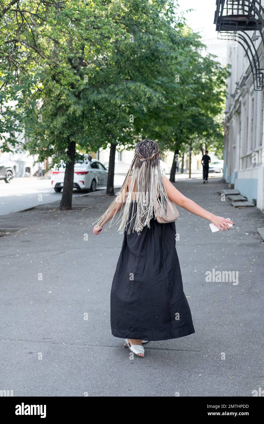 A girl in a black dress and long afro-braids is spinning and walking ...
