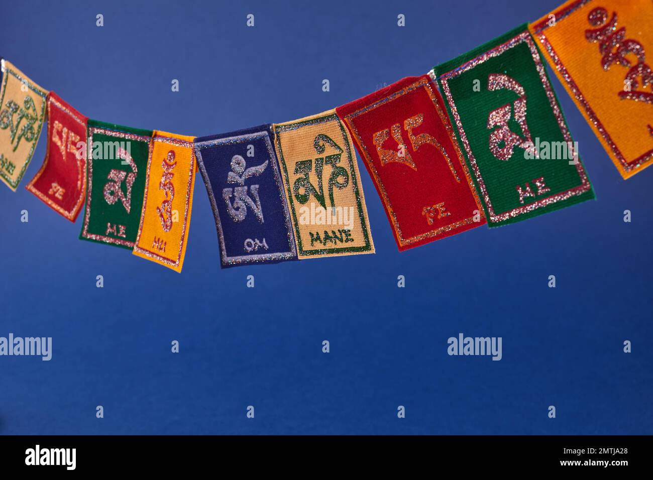 Tibetan Buddhist flags against blue background. Text on flags Om mani padme hum meaning The