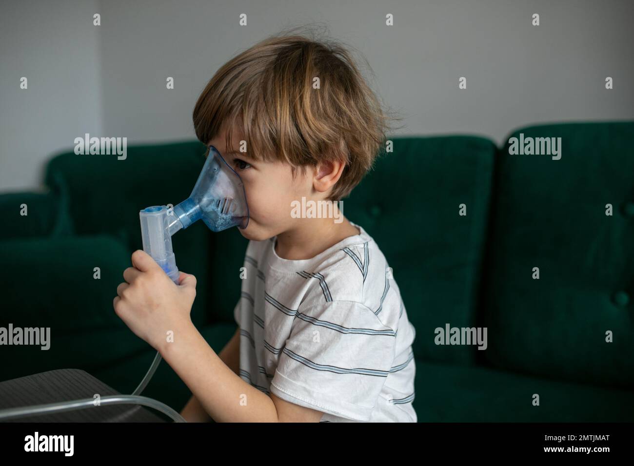 Calm, tired blonde little boy breathing with nebulizer, inhaler mask