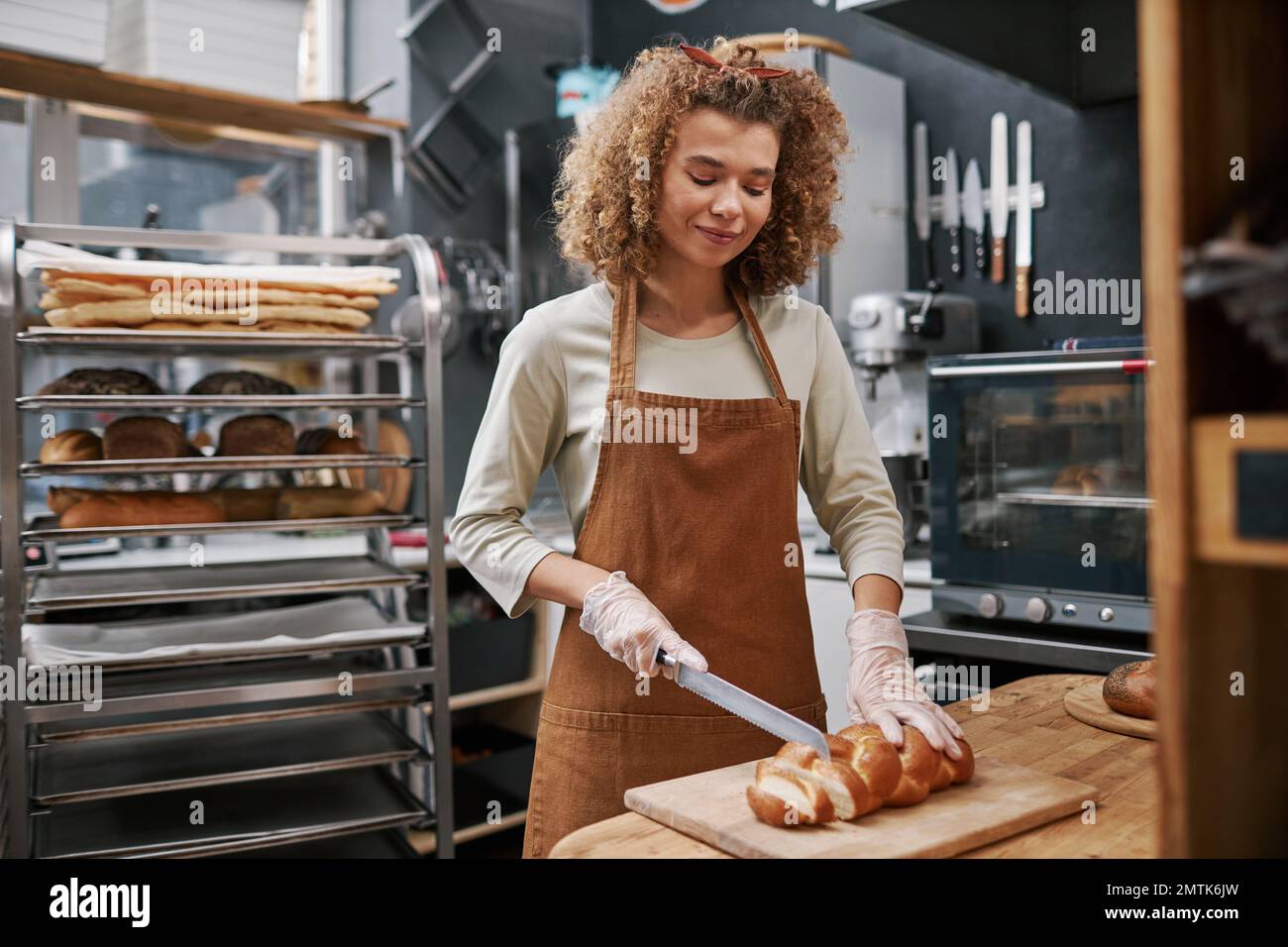 Smiling baker wearing gloves when cutting bread for customers Stock Photo