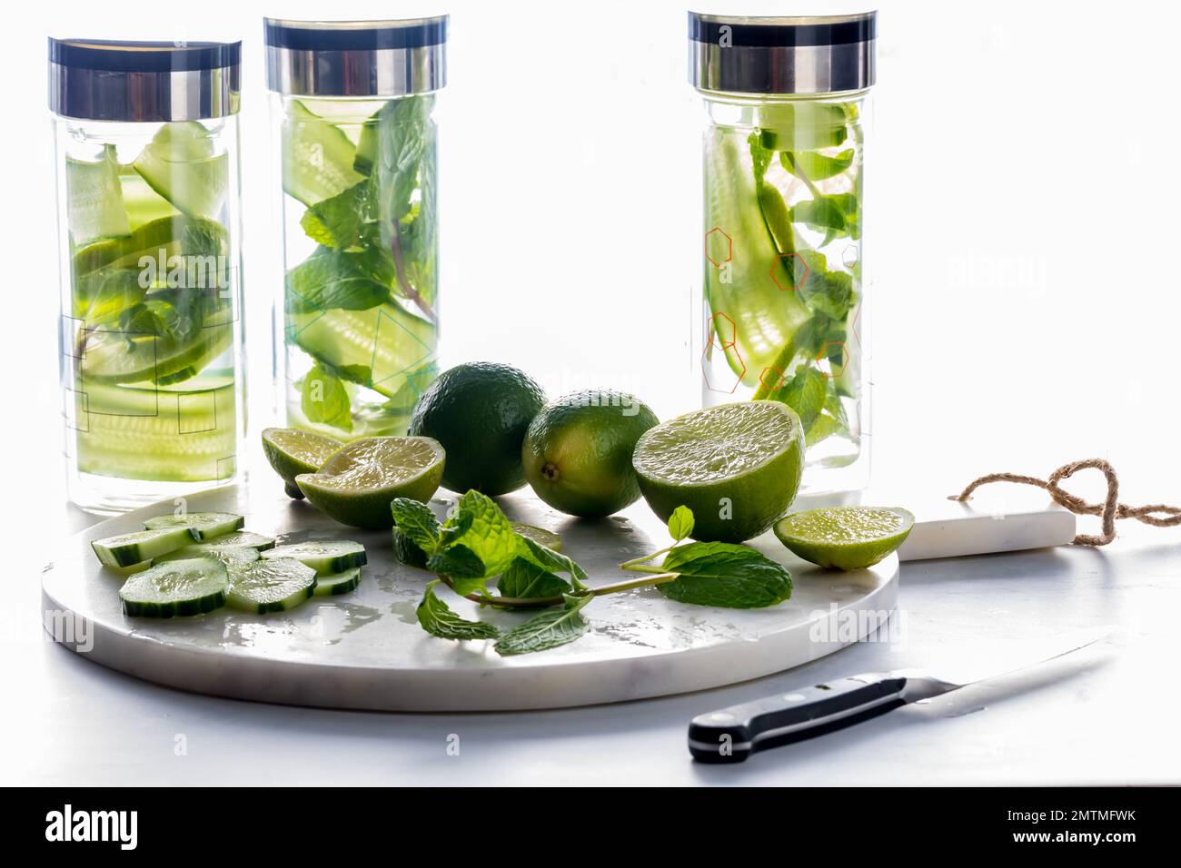 Glass bottles of cucumber water with ingredients on a marble slab in front. Stock Photo