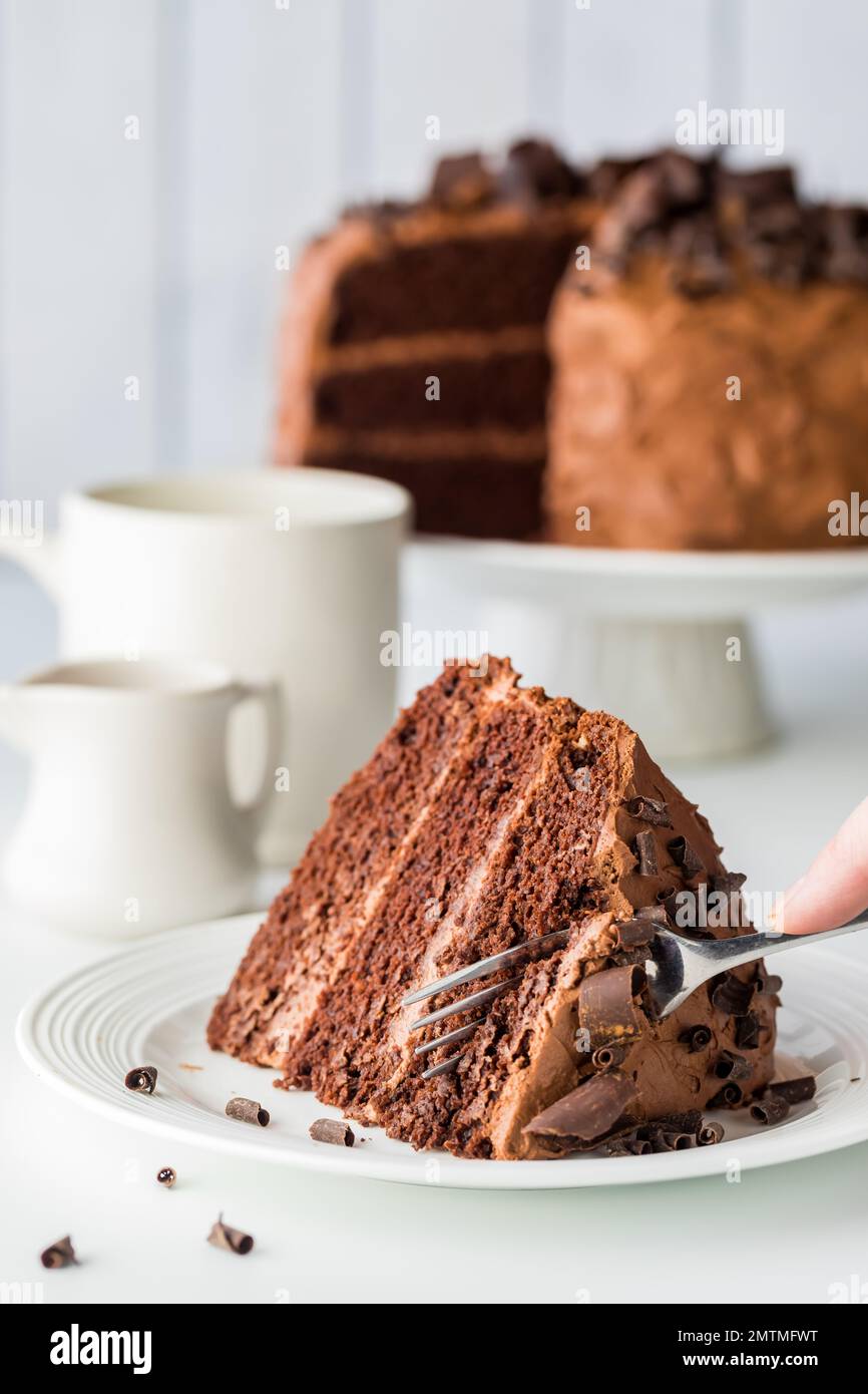 A slice of decadent chocolate cake with a hand holding a fork cutting into it. Stock Photo