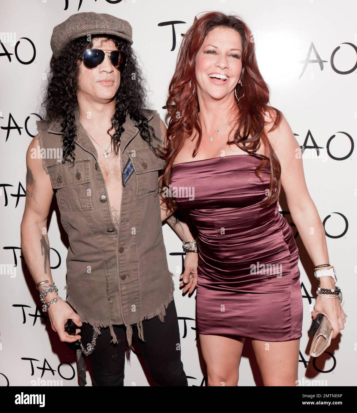 Legendary musician Slash aka Saul Hudson shows off his tattoos in a ripped unbuttoned vest as he poses on the red carpet with his voluptuous wife Perla Ferrar at TAO Nightclub inside