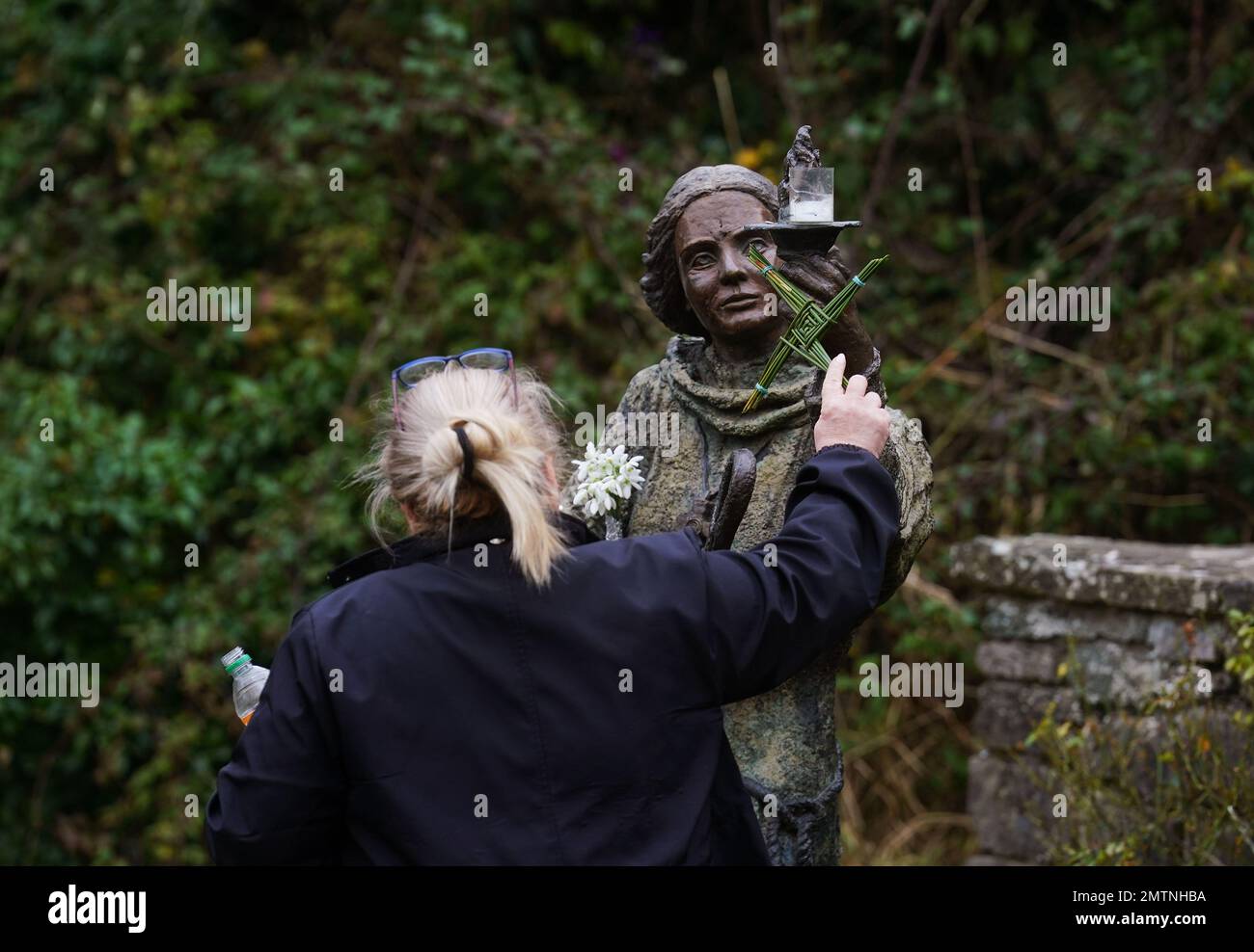 A woman holds a traditional St. Brigid's Cross made from rushes up to a statue of St. Brigid at St Brigid's holy well in Co Kildare. February 1st marks St Brigid's Day which is seen by many in Ireland as the first day of Spring. Picture date: Wednesday February 1, 2023. Stock Photo
