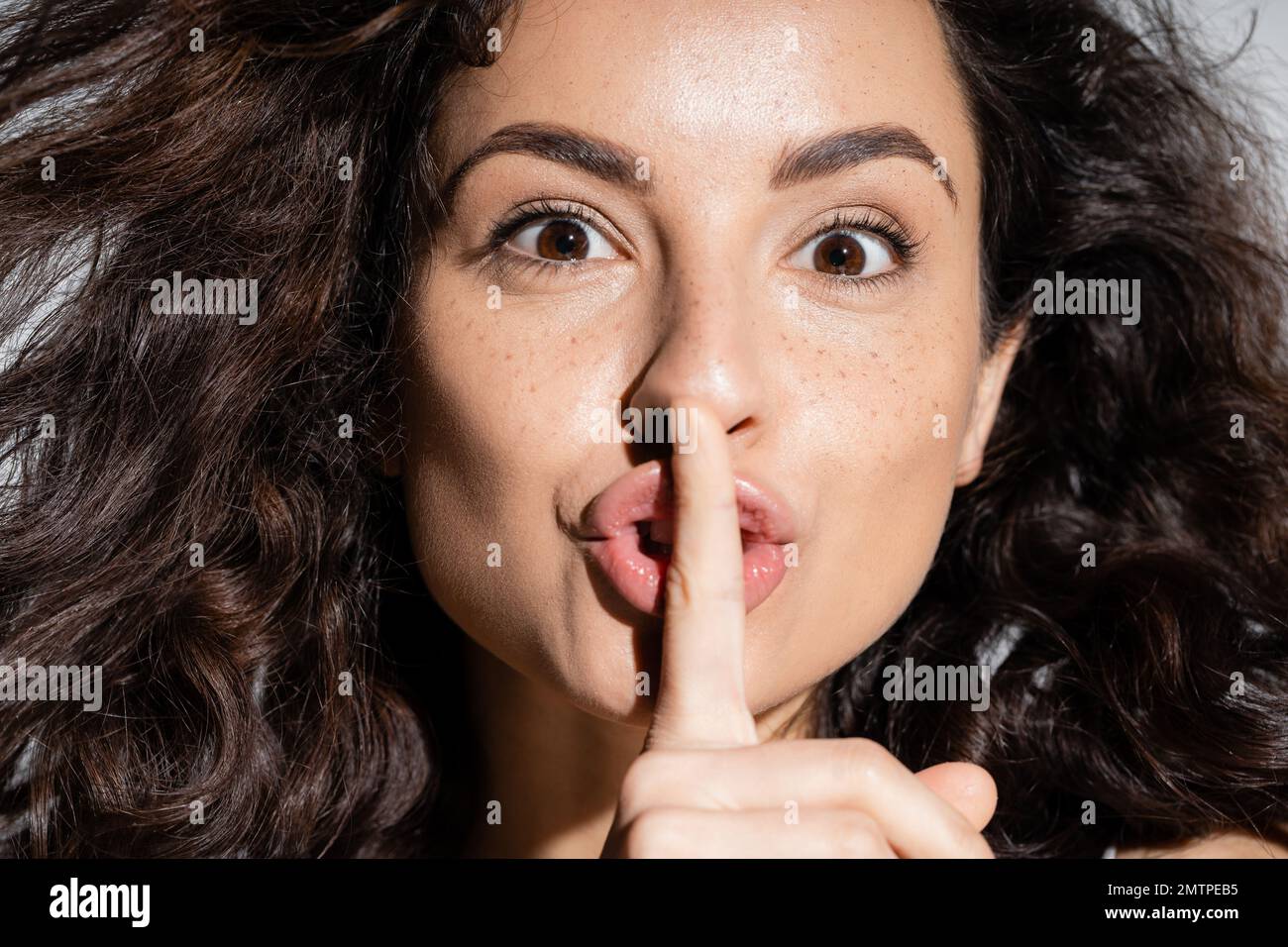 Portrait of curly freckled woman showing secret gesture isolated on grey,stock image Stock Photo