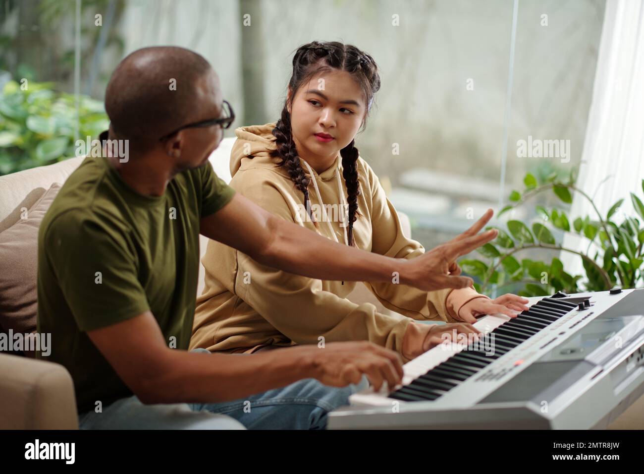 Music teacher explaining teenage girl who to play synthesizer Stock