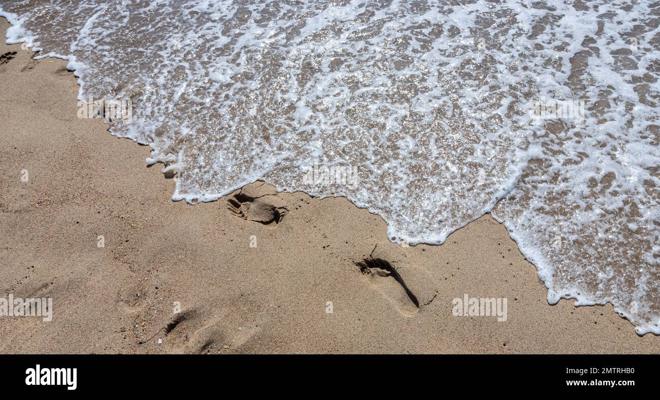Footprints of a man on the yellow beach sand from walking barefoot by the sea with water that washes away the footprints. Contemplation of life Stock Photo