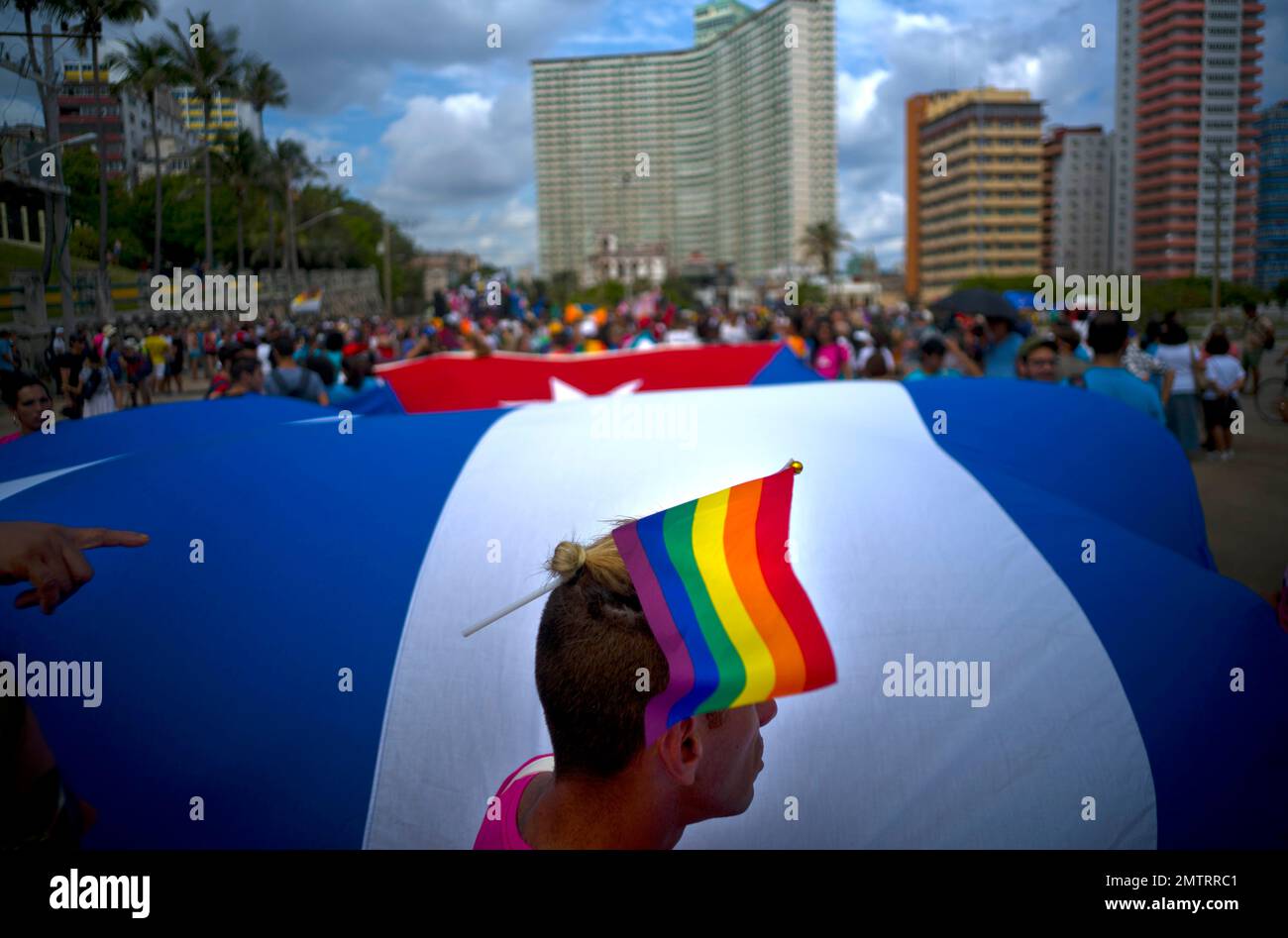 A man wears a rainbow hand flag on his head backdropped by Cuban's ...