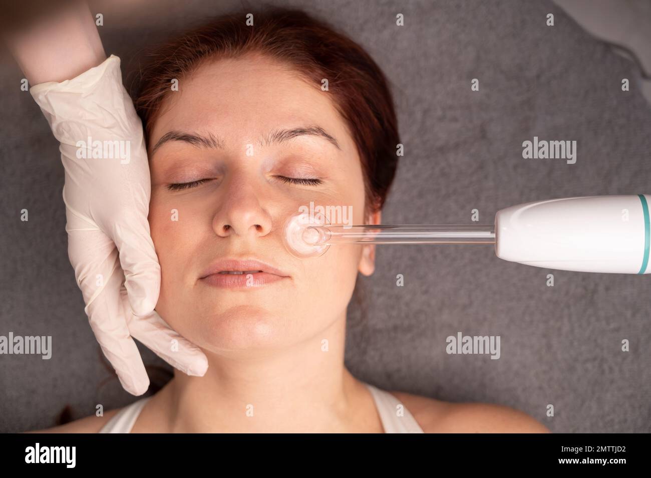 The doctor uses the darsonval apparatus against acne on the face of a