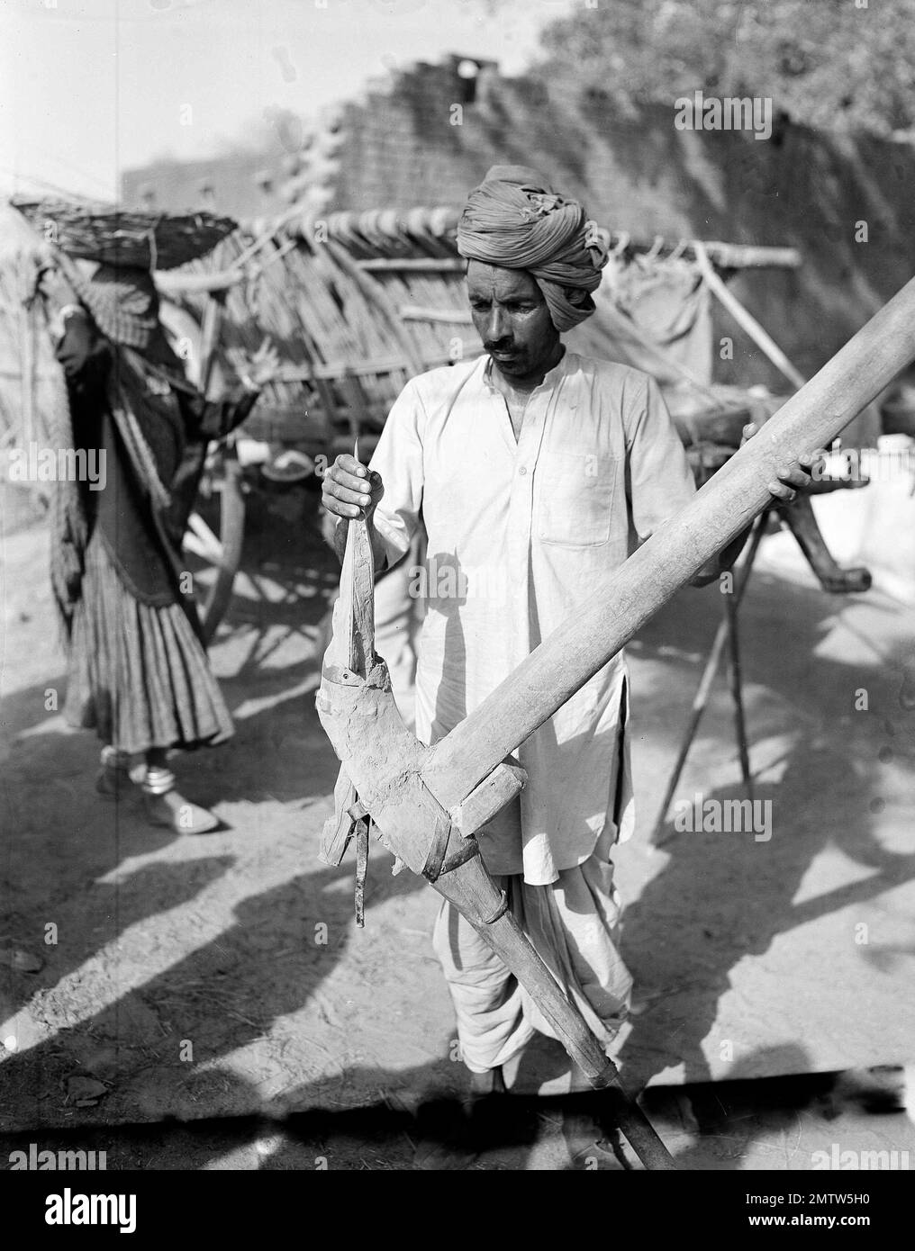 A farmer of India scrapes the mud off his ancient plowshare on his farm
