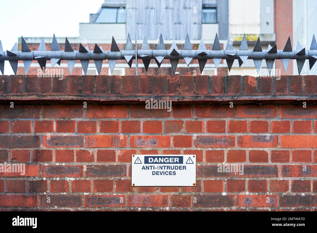 Red brick wall with rotating spike anti intruder device and warning sign Stock Photo