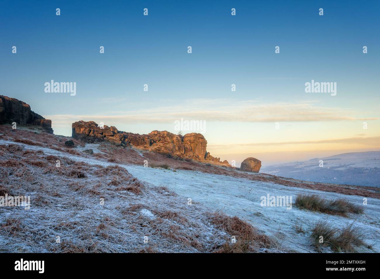 A stunning sunrise landscape at the Cow and Calf Rocks above Ilkley with the sun just hitting the rock face on a very cold day with frost covering the Stock Photo