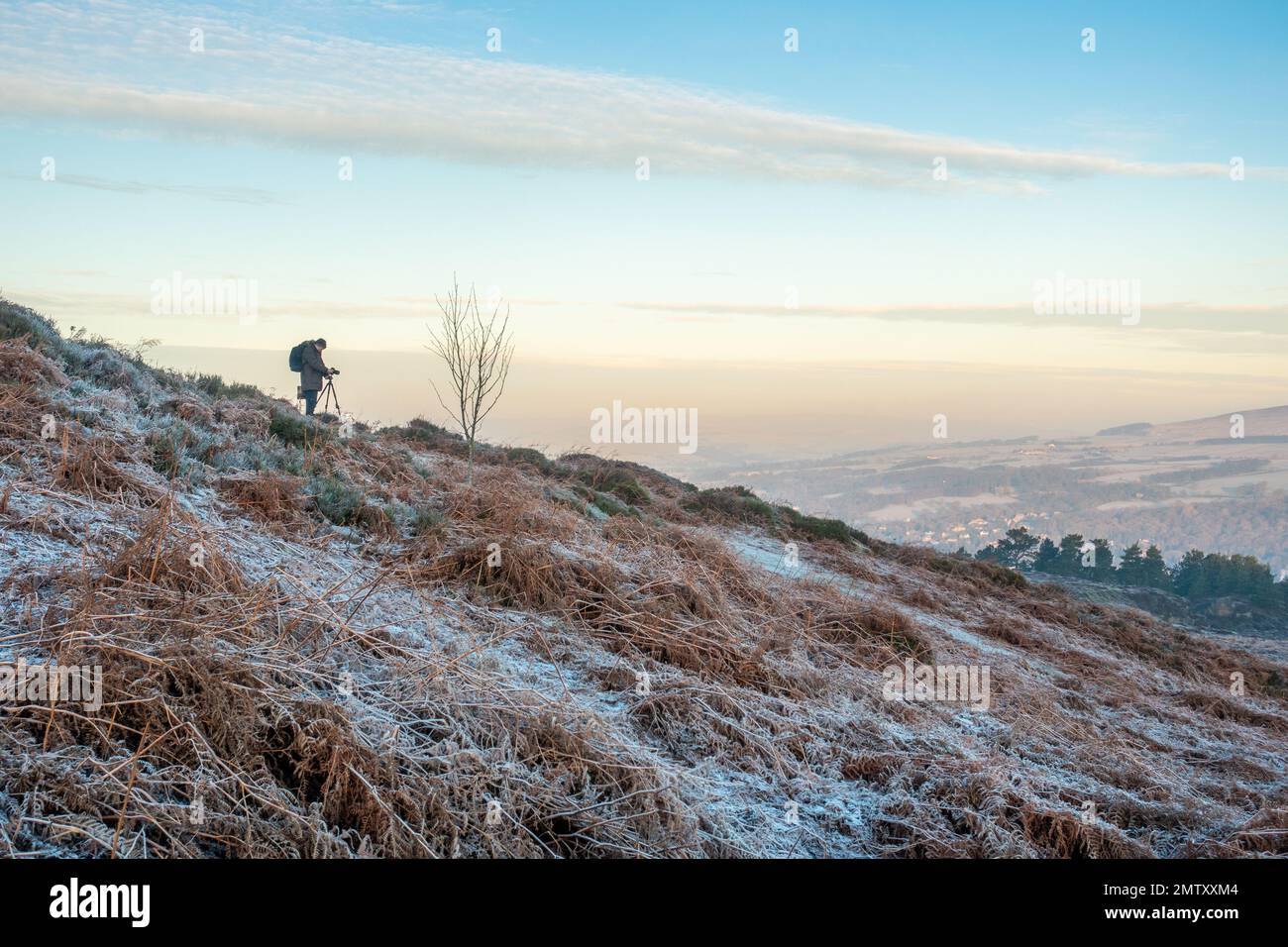 Photographer using a tripod and taking sunrise landscape photos on Ilkley Moor on a very cold day with frost covering the ground in West Yorkshire, En Stock Photo